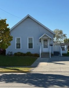 The ECBDD Tech Home visible from the street. A large, light grey house with a driveway and lawn against a blue sky