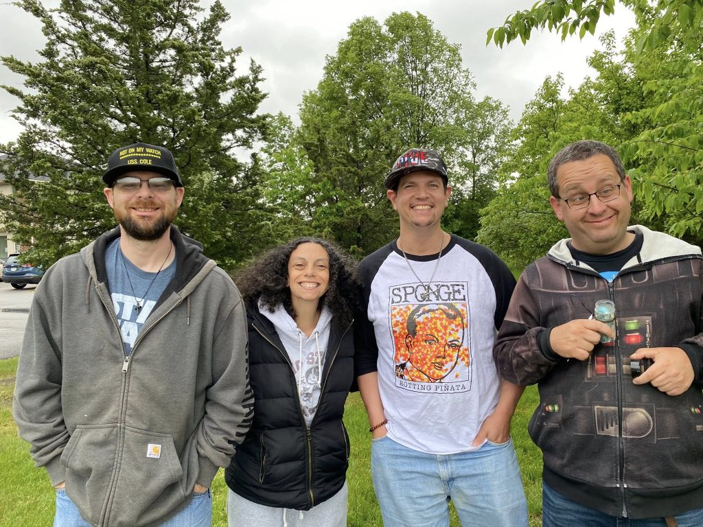 Four adults standing in a group outside with trees in the background