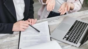 Two women sitting at a computer with paperwork